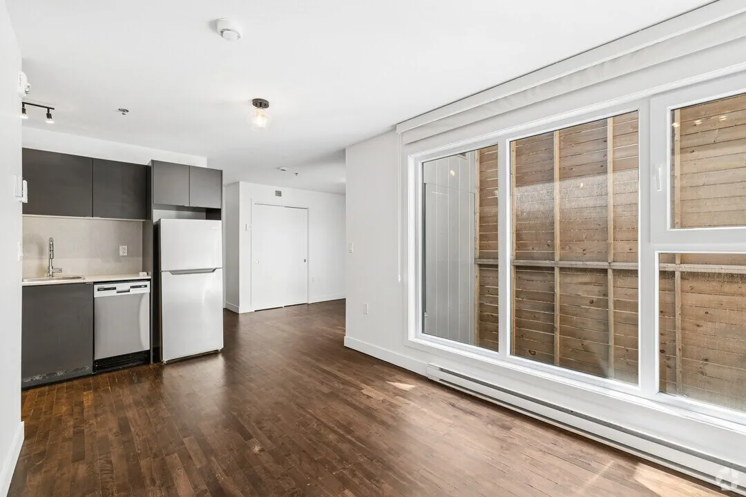 Intérieur d'un studio : cuisine ouverte, planchers de bois franc et porte coulissante vers une terrasse privée