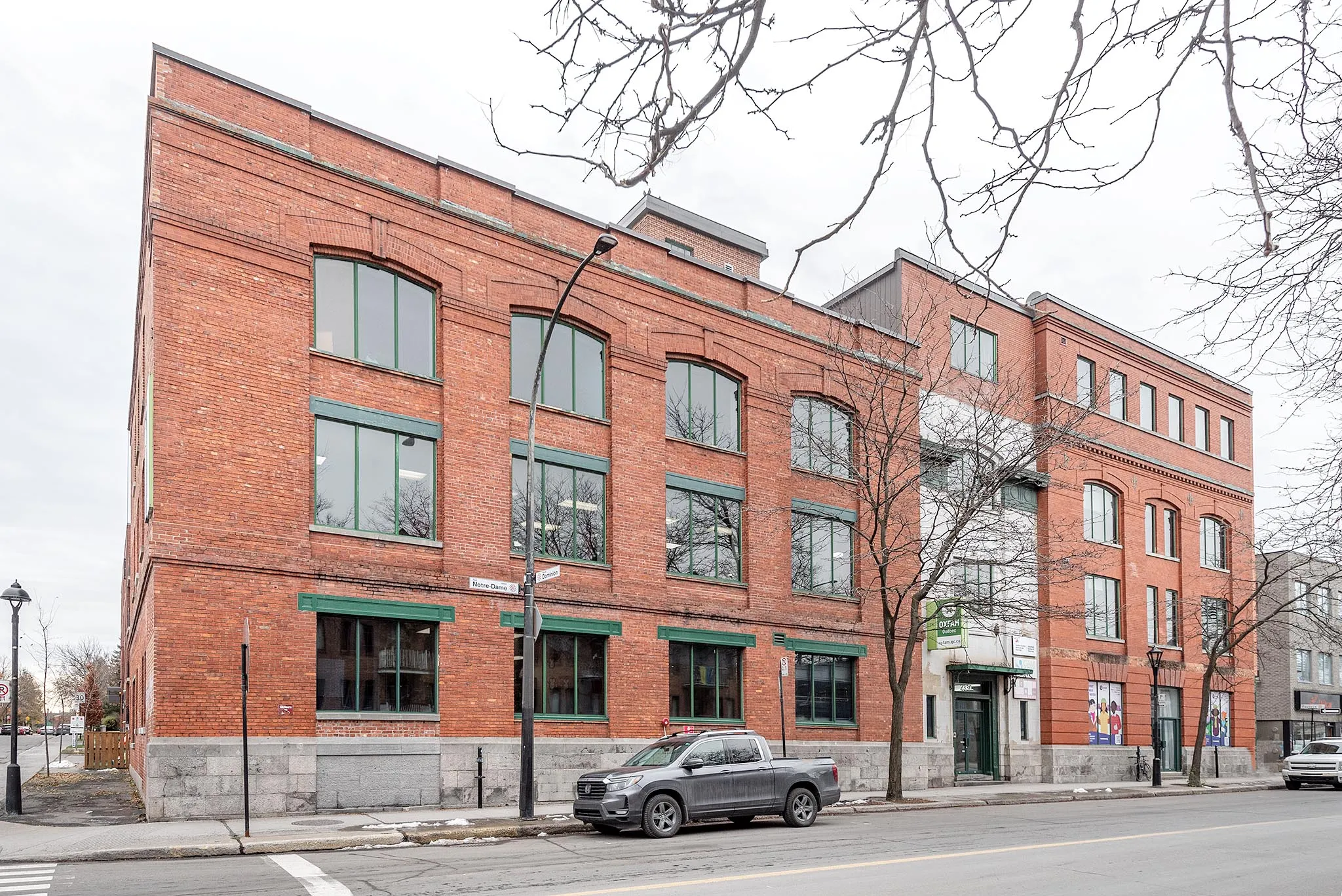 2330 Notre-Dame Ouest: red brick industrial building with arched, green-framed windows, at the corner of rue Dominion